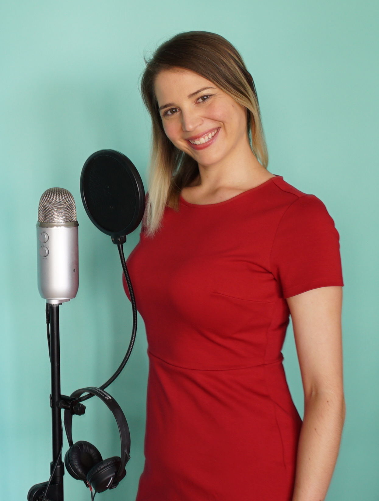 Emily Milling in red dress smiling beside a blue yeti microphone