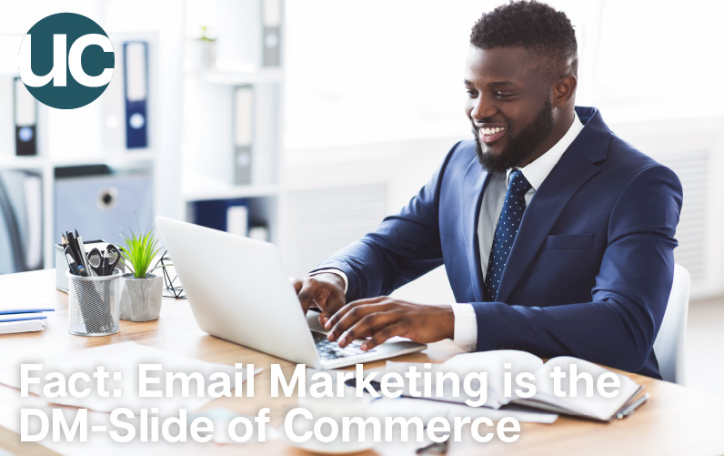 Fact: Email Marketing is the DM-Slide of Commerce - Featured Image: A man in a blue suit sits at his desk smiling at his computer.