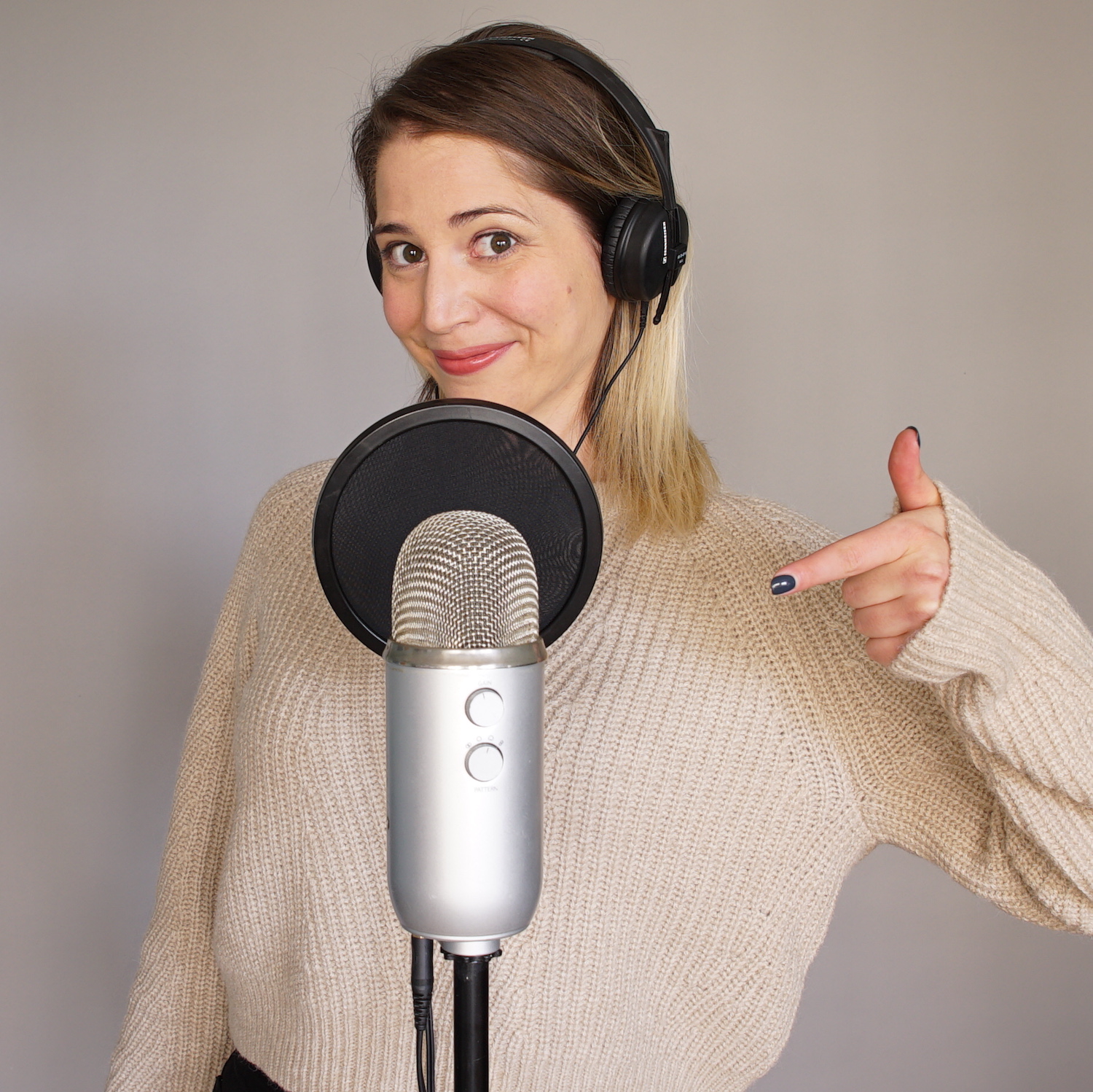 Emily milling pointing at blue yeti mirophone wearing beige sweater