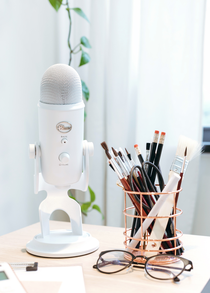 White yeti podcast microphone on desk beside pencils and nerdy glasses